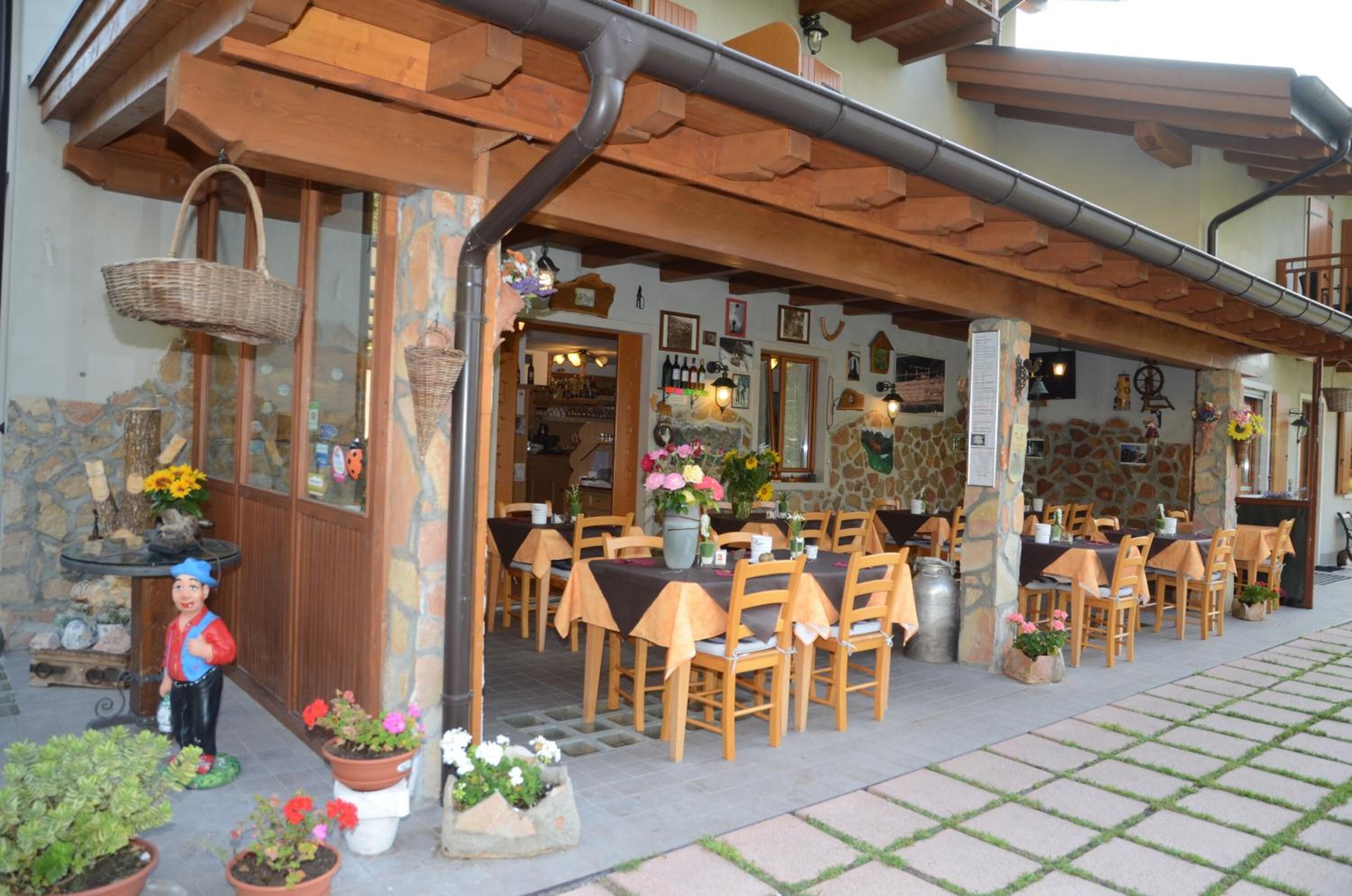 An outdoor dining area with wooden tables and chairs, stone walls, and potted plants.