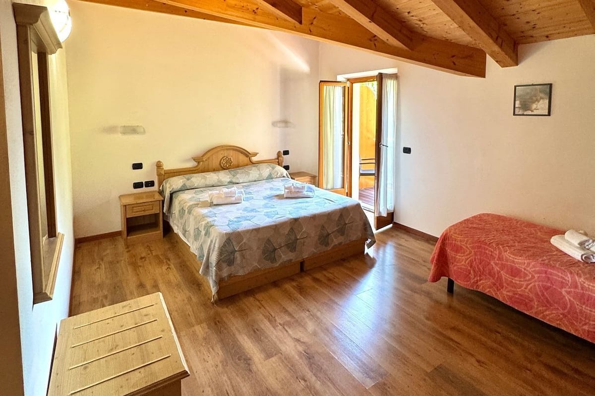 Une chambre avec un plafond en bois, un lit recouvert d’une couvre-lit à motifs floraux, une table de chevet et un couvre-lit rouge sur le lit adjacent.