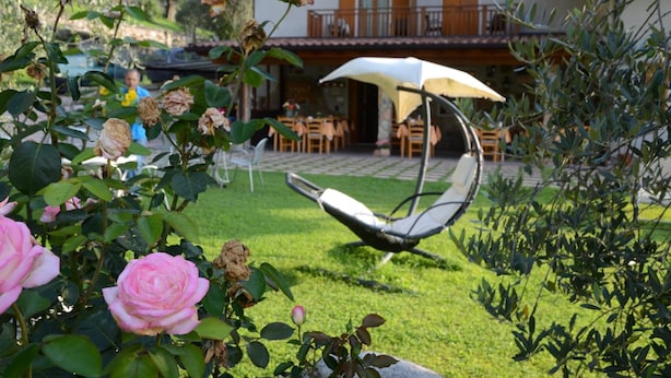 A garden with roses, a chair, and a building with outdoor seating. - Agriturismo Girardelli (Riva del Garda)