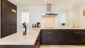 Une cuisine moderne avec des meubles de couleur sombre, un plan de travail blanc, une hotte en acier inoxydable et une fenêtre agrémentée de rideaux blancs.