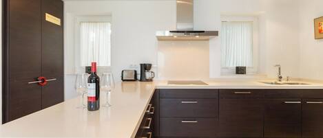 Una cocina moderna con armarios oscuros, encimera blanca, extractor de acero inoxidable y una ventana con cortinas blancas.