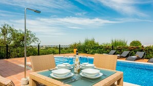 Un espace de restauration en plein air avec une table dressée pour quatre personnes, donnant sur une piscine.