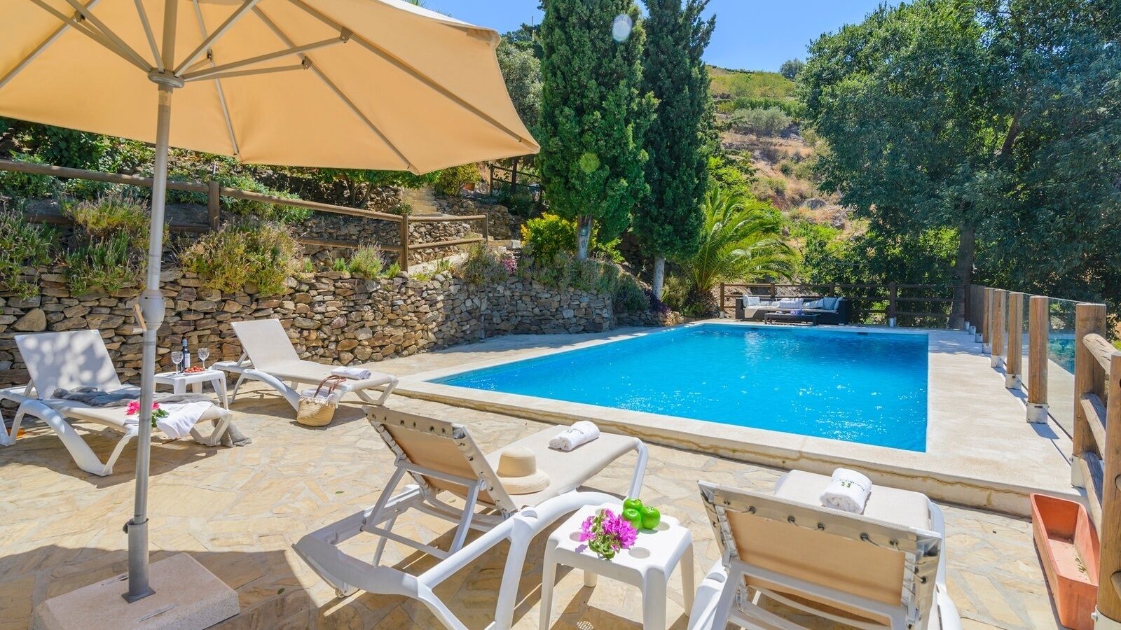 Un espace piscine avec des chaises longues, une table avec des boissons et un mur en pierre.
