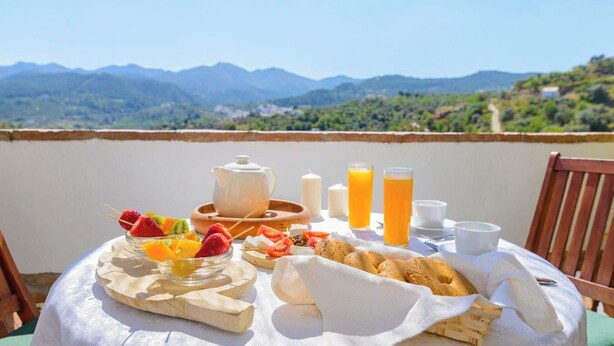 A breakfast setup with fruit skewers, pastries, and beverages on a table with a mountain view.