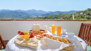 Ein Frühstückstisch mit Obstspießen, Gebäck und Getränken, mit Blick auf die Berge.