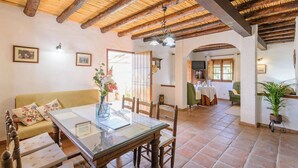 A dining area with a glass table, wooden chairs, a sofa with floral cushions, and a ceiling with exposed beams.