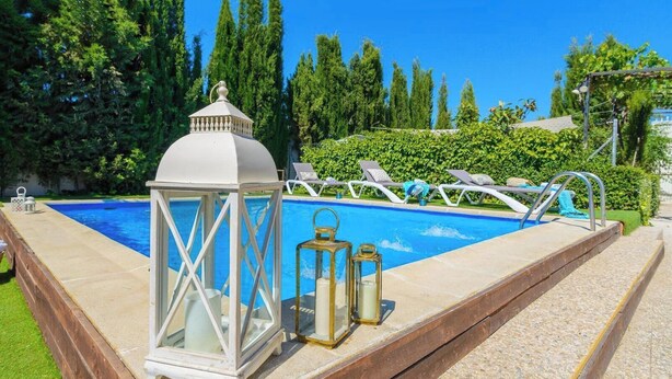 Une piscine agrémentée d’une lanterne blanche et de bougies, entourée de chaises longues et de verdure.