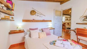 Une chambre confortable avec un lit, des oreillers, une table de chevet avec une lampe, une étagère en bois avec des livres et une décoration murale rustique.