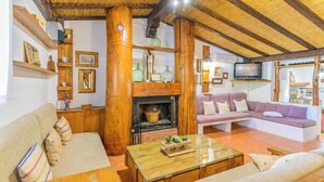 Un salon chaleureux avec une cheminée, des poutres en bois, un canapé et un téléviseur.