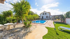 A pool area with a stone patio, a white house in the background, and a clear sky. - Loma el Letrao Almogía by Ruralidays (Málaga)