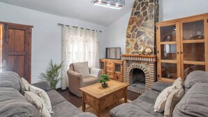 A cozy living room with a stone fireplace, a wooden cabinet, and a comfortable sofa. - Herrero El Borge by Ruralidays (Málaga)