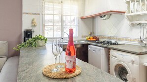 A kitchen with a washing machine, a bottle of red wine, and two glasses on a woven mat. - Mulera Alozaina by Ruralidays (Málaga)