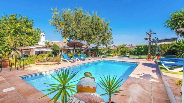 A swimming pool with lounge chairs, a small building, and surrounding greenery. - Villa Muñoz Ronda by Ruralidays (Málaga)