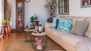 A cozy living room with a beige sofa, a coffee table, and a small side table. There are decorative pillows, a vase with flowers, and a potted plant. - Villa Muñoz Ronda by Ruralidays (Málaga)