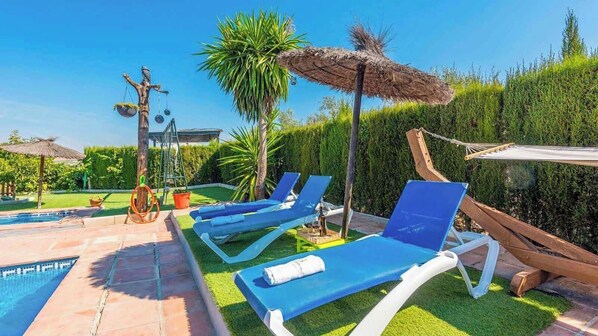 A poolside area with blue lounge chairs, a thatched umbrella, and a wooden swing. - Villa Muñoz Ronda by Ruralidays (Málaga)