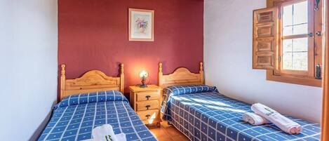A bedroom with two beds, wooden headboards, a nightstand with a lamp, and a window with wooden shutters.