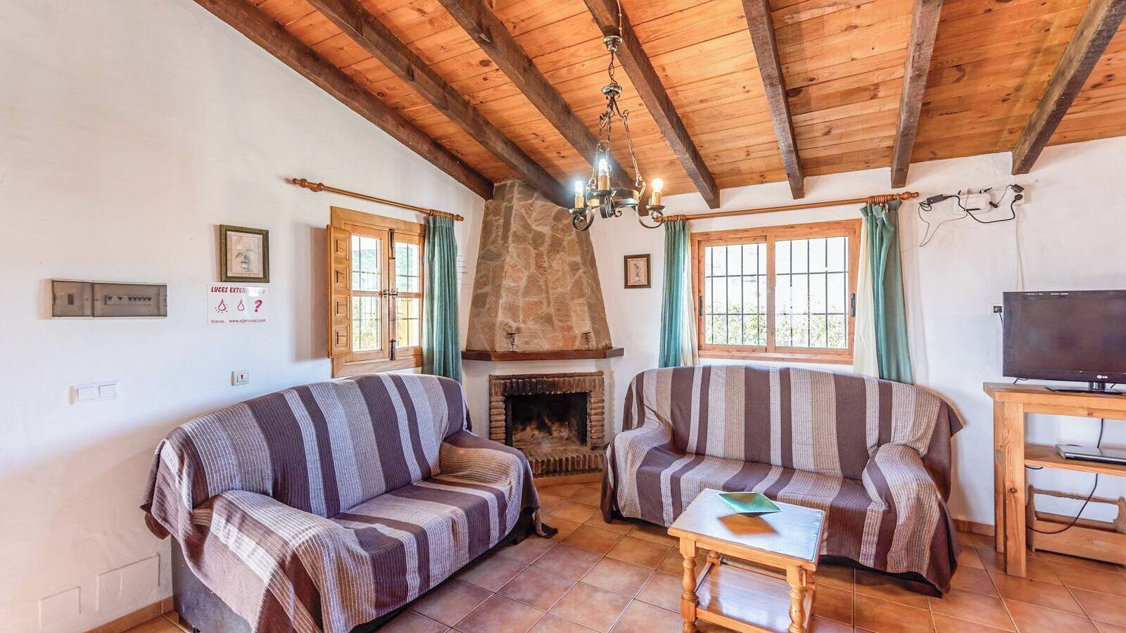 A cozy living room with two striped sofas, a stone fireplace, wooden beams, and a television on a wooden stand.