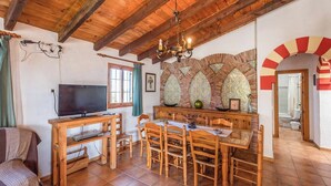 A cozy room with a wooden dining table, chairs, a television, and a stone wall with arches.