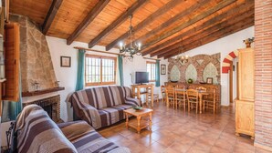 A cozy living room with a fireplace, wooden furniture, and a dining area with a brick wall and decorative arch.