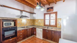 A kitchen with wooden cabinets, a built-in oven, a microwave, a dishwasher, and a window with a decorative frame. - Poniente Almáchar by Ruralidays (Málaga)