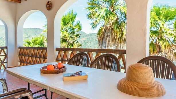 A table with a woven hat, a book, and a fruit bowl with oranges and a glass. - Poniente Almáchar by Ruralidays (Málaga)