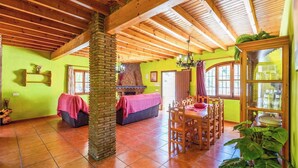 A cozy room with a wooden ceiling, a brick pillar, a dining table with chairs, a sofa, and a fireplace. - Poniente Almáchar by Ruralidays (Málaga)