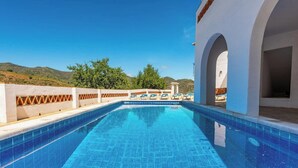 A swimming pool with clear blue water, surrounded by white walls and arches, with a view of hills and trees in the background. - Poniente Almáchar by Ruralidays (Málaga)