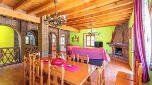 A dining area with a wooden table and chairs, a fireplace, and a balcony with a wooden railing. - Poniente Almáchar by Ruralidays (Málaga)