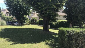 A well-maintained grassy area with mature trees and a stone building in the background. - Nice apartment Uzès center (Uzès)