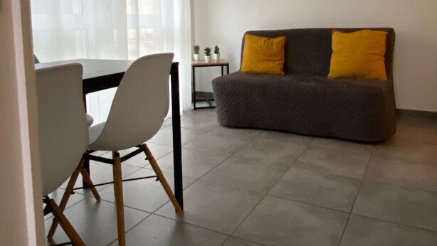 A living room with a grey sofa and yellow cushions, a dining table with chairs, and a small side table with decorative items. - Nice apartment Uzès center (Uzès)