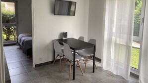 A modern room with a dining table, chairs, a TV mounted on the wall, and a large window with sheer curtains. - Nice apartment Uzès center (Uzès)