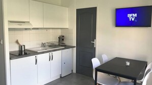 A modern kitchen with white cabinets, a black countertop, and a small dishwasher. There is a dining table with four chairs and a flat-screen TV mounted on the wall. - Nice apartment Uzès center (Uzès)