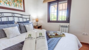 A neatly made bed with a tray of coffee and pastries, a bedside table with a lamp, and a window with a view of greenery. - Cortijo del Abuelo El Gastor by Ruralidays (Cádiz)