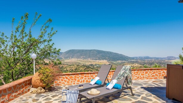 A terrace with two sun loungers, a stone wall, and a view of distant hills. - Cortijo del Abuelo El Gastor by Ruralidays (Cádiz)