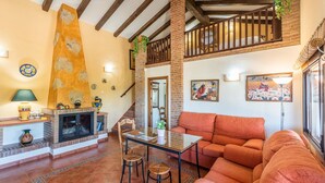 A cozy living room with a fireplace, a sofa, a dining table, and a staircase leading to an upper level. - Cortijo del Abuelo El Gastor by Ruralidays (Cádiz)