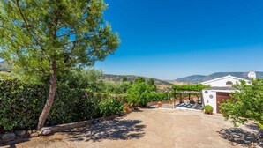 A villa with a paved driveway leading to a covered outdoor area, surrounded by lush greenery and a view of distant hills. - Cortijo del Abuelo El Gastor by Ruralidays (Cádiz)