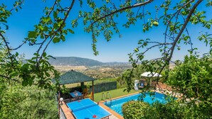 A pool area with a view of distant hills, a covered seating area, and a table with chairs. - Cortijo del Abuelo El Gastor by Ruralidays (Cádiz)