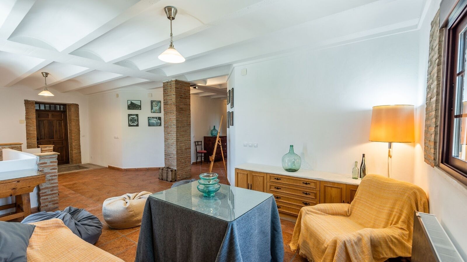 A spacious living room with a high ceiling, a fireplace, a dining area with a table and chairs, and a cozy seating area with a lamp.