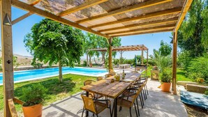 A covered outdoor dining area with a pool and lush greenery in the background. - Caserío Lo Bulle Oria by Ruralidays (Almería)