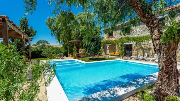 A rectangular swimming pool with a white deck, surrounded by lush greenery and a stone building with a tiled roof. - Caserío Lo Bulle Oria by Ruralidays (Almería)