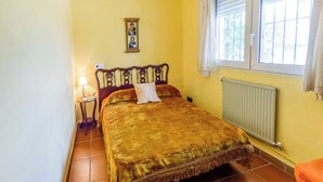 Une chambre à coucher avec un lit, une table de chevet, une lampe, une fenêtre avec des rideaux et un radiateur.
