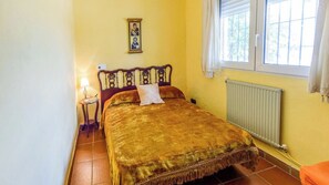 A bedroom with a bed, a nightstand, a lamp, a window with curtains, and a radiator.