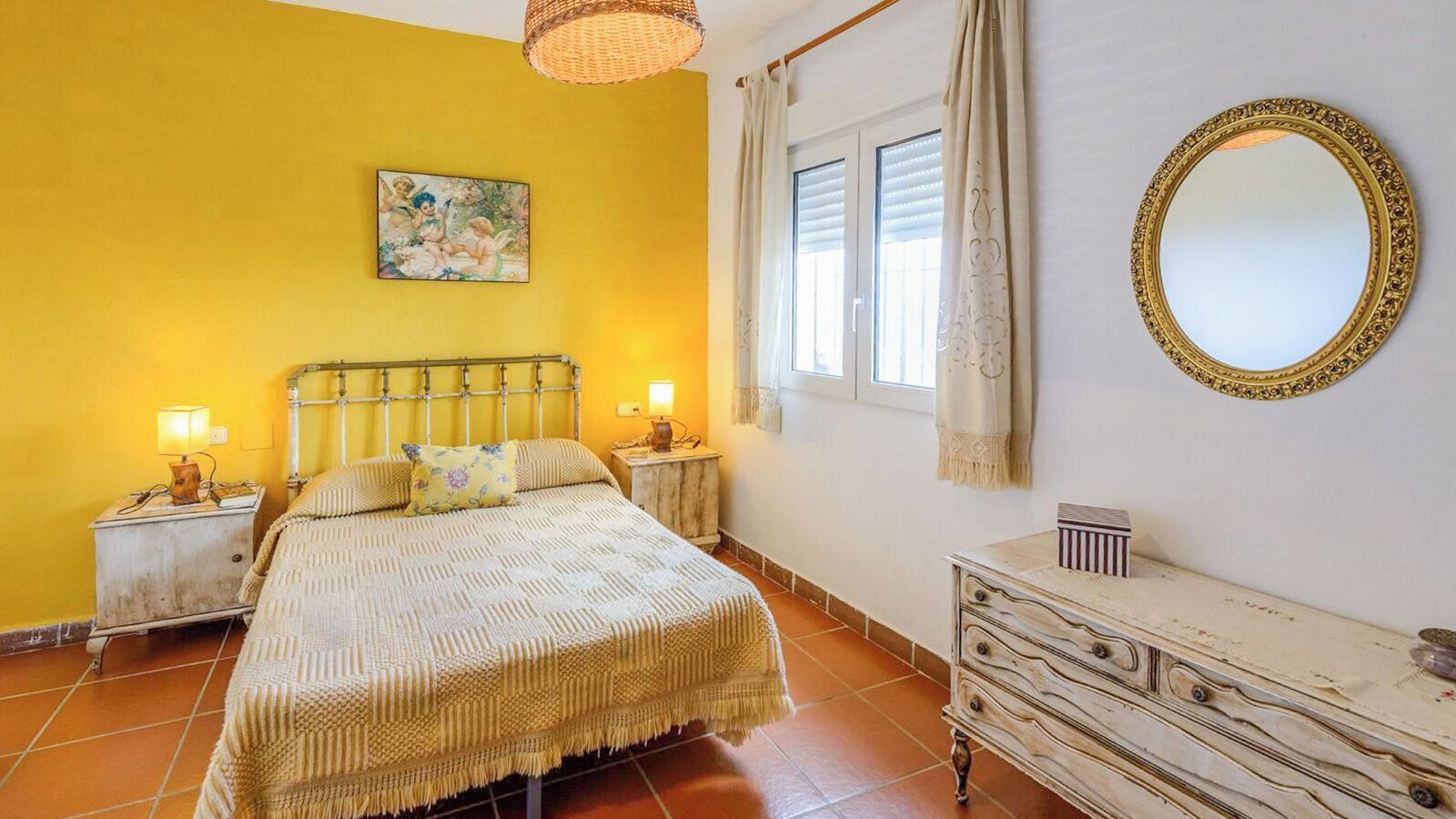 A bedroom with a bed, bedside tables, a dresser, a mirror, and a window with curtains.