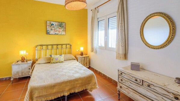A bedroom with a bed, bedside tables, a dresser, a mirror, and a window with curtains.