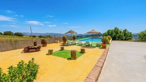 An outdoor pool area with lounge chairs, a barbecue grill, and a view of mountains.