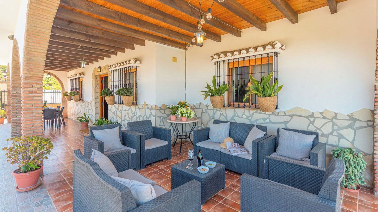 An outdoor patio with wicker furniture, stone walls, and potted plants.