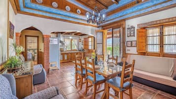 A spacious living area with a dining table, wooden chairs, a sofa, and a kitchen in the background.