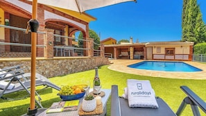 Zona de piscina con sillas de descanso, una mesa con frutas y una botella, y una toalla con el logotipo de 'ruraldays'.