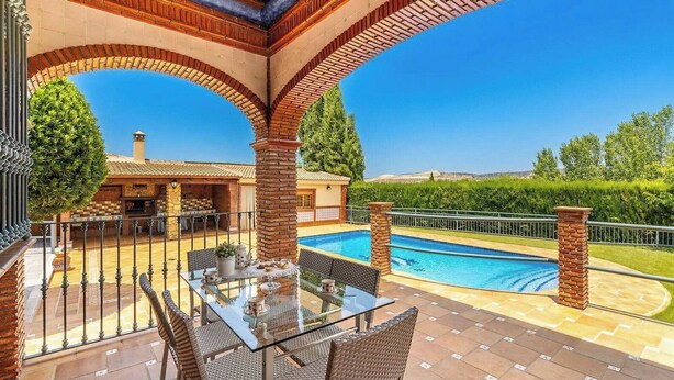 Un espace aménagé au bord de la piscine, avec une table en verre, des chaises et une arche en briques.