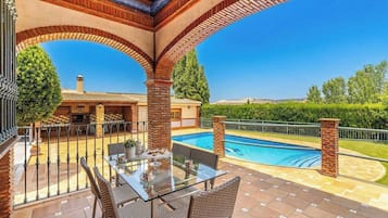 A poolside area with a glass table, chairs, and a brick archway.